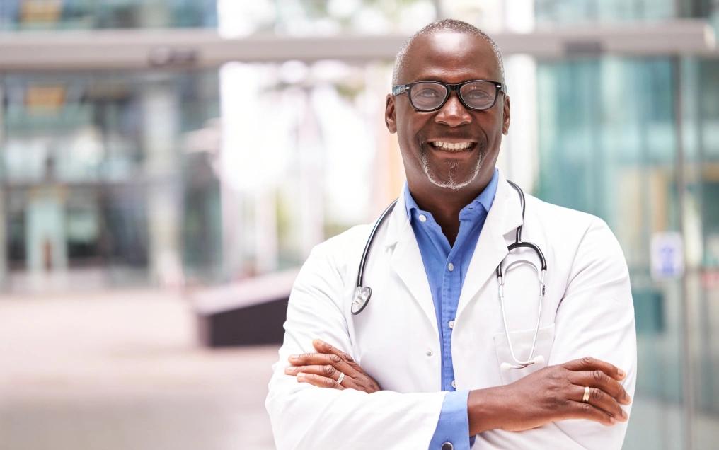 Smiling Black doctor crossing his arms and wearing glasses and a lab coat.